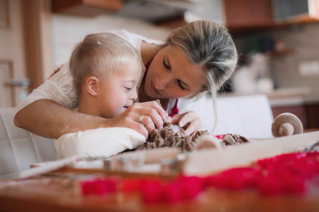 A happy handicapped down syndrome child with his mother indoors baking.